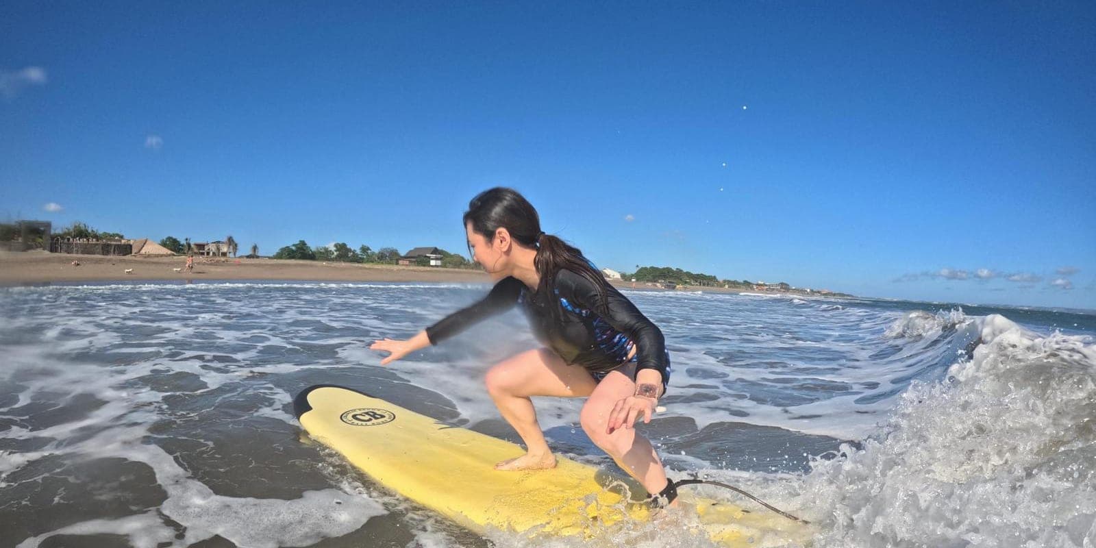 A student riding a soft-top board through the whitewater at Berawa Beach, arms out for balance