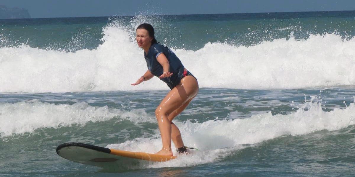 A student riding a yellow soft-top through the shallows, throwing peace signs at the camera