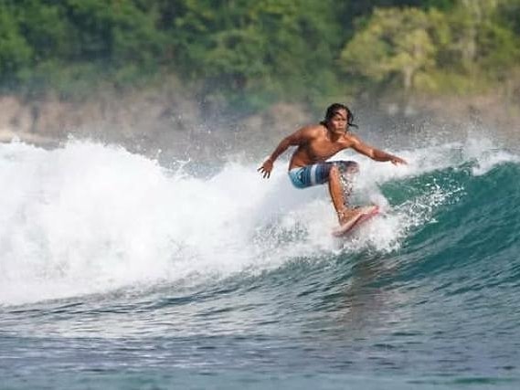 A surfer carving along the face of a clean wave at Berawa Beach, jungle-covered headland behind him