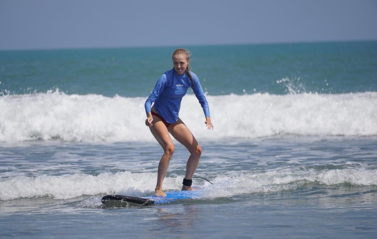 A first-time surfer standing up on a soft-top board in the whitewater at Berawa Beach