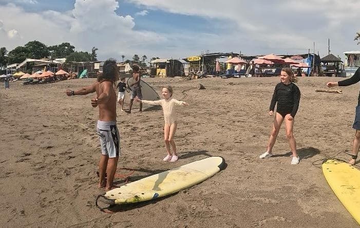 An instructor running a pop-up drill on the sand with a small group, boards laid out beside them